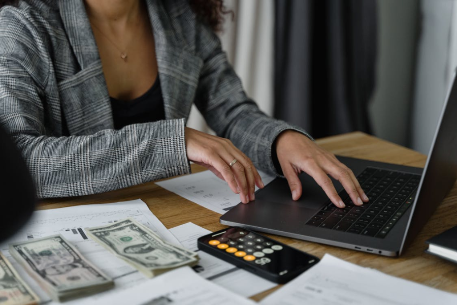 Person working with a laptop and a smartphone, with documents and money on the table