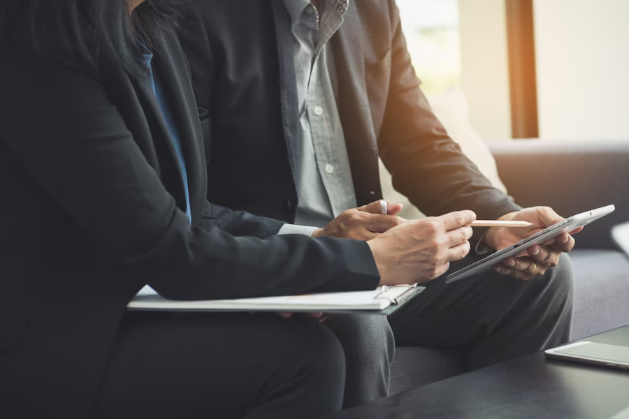 people in business attire discussing something with folders, tablets, and computers around